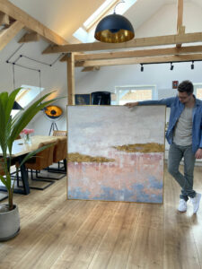 Das Bild zeigt eine Person, die ein großes Gemälde in der Hand hält